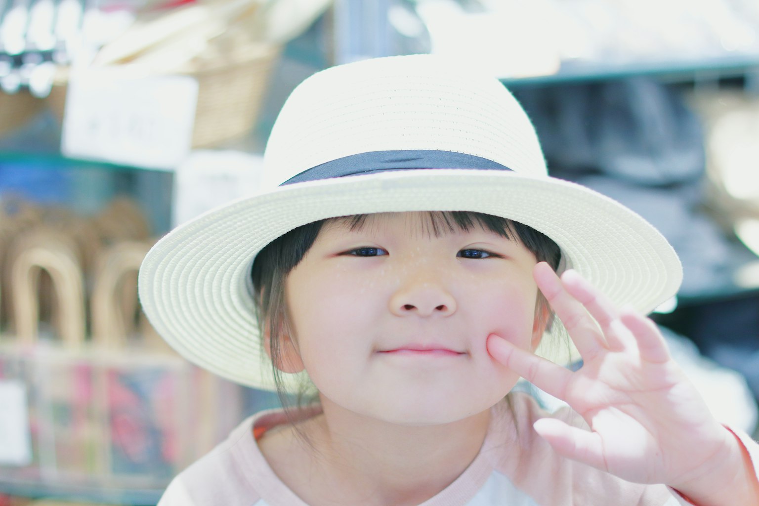 Enfant portant un chapeau blanc souriant et faisant un signe de la main