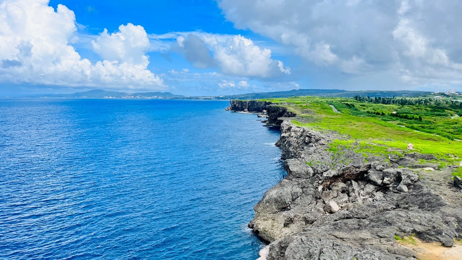 Pemandangan tebing dengan lautan biru dan awan putih padang hijau