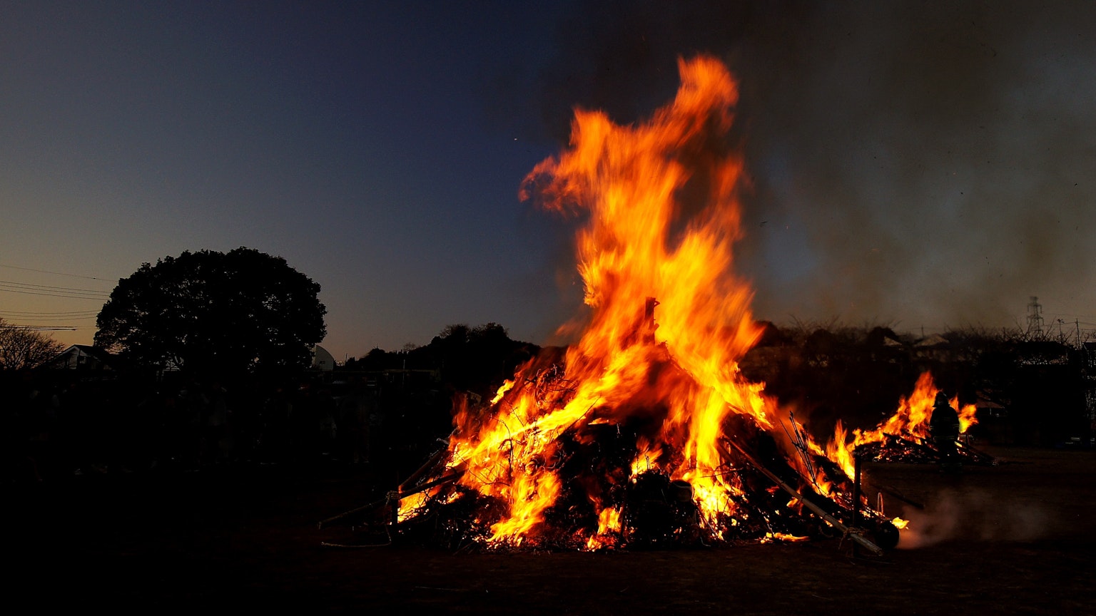 Großes loderndes Feuer in der Dämmerung mit umliegenden Bäumen