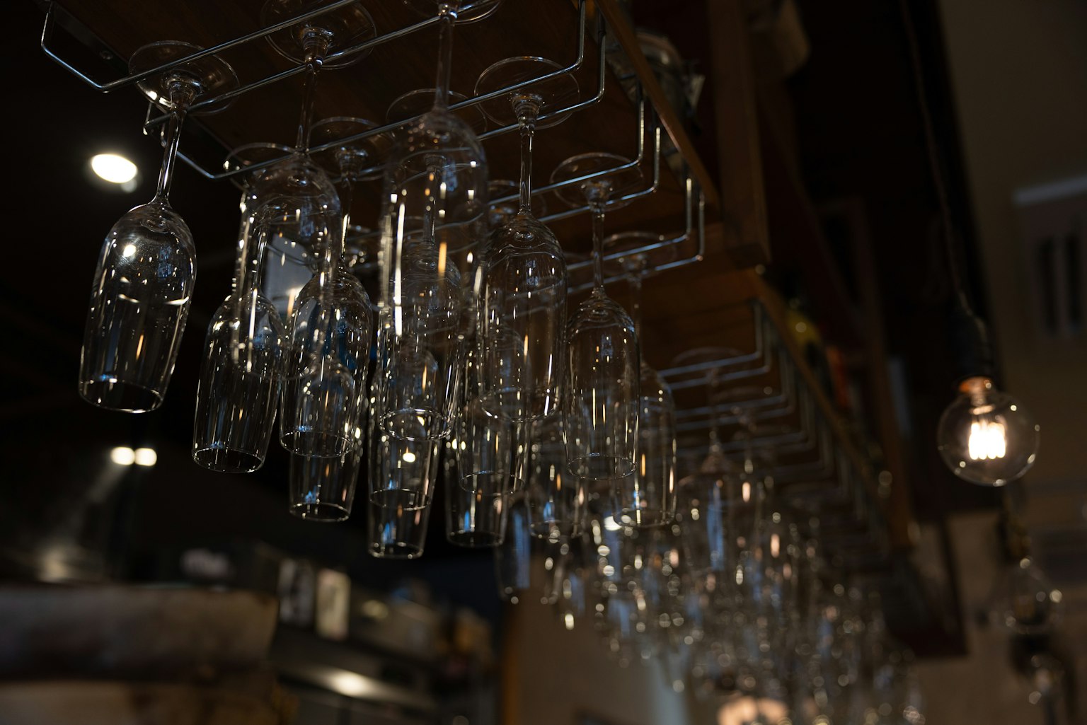 Bicchieri trasparenti appesi a un supporto da bar in un ambiente poco illuminato