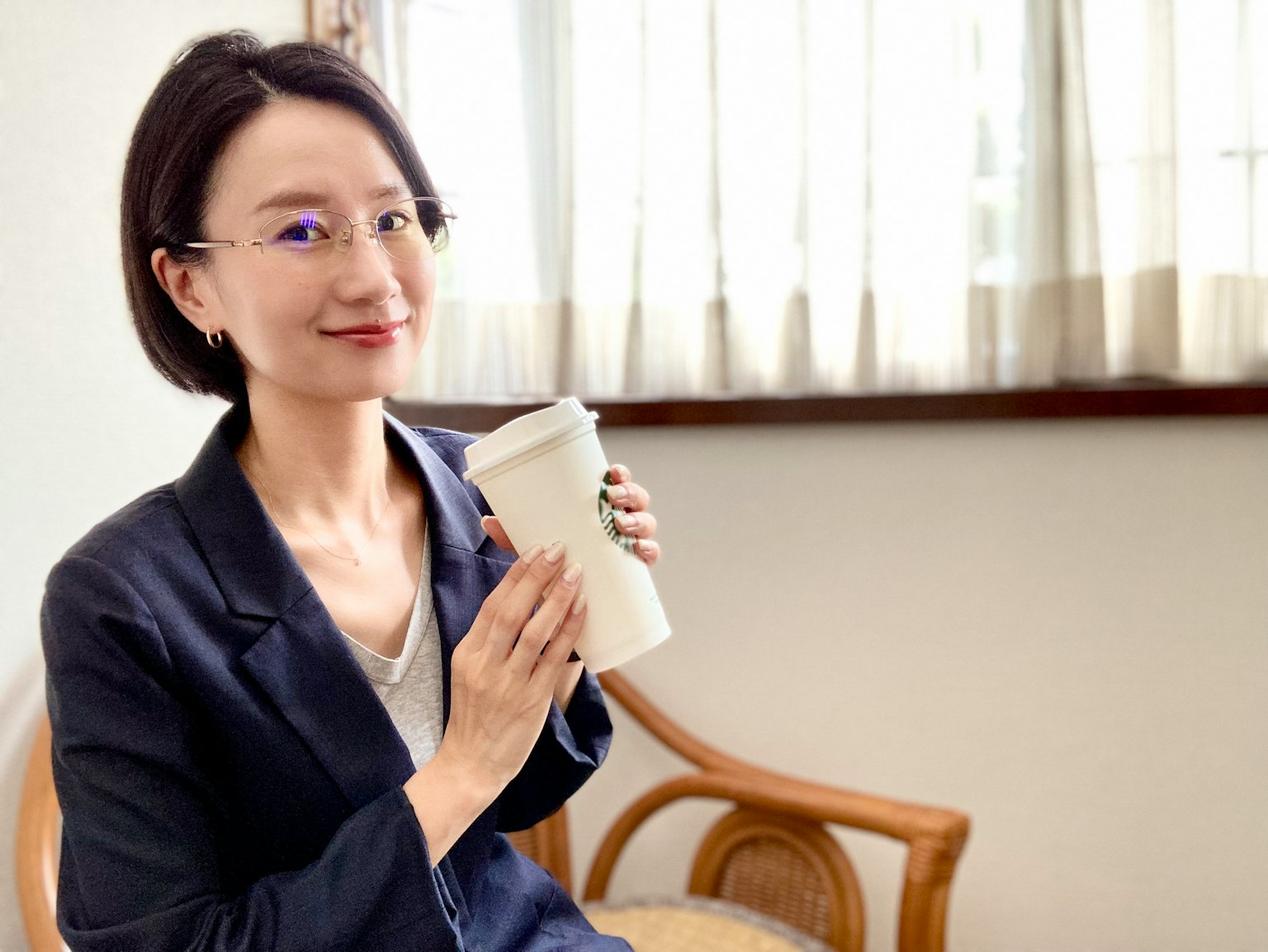 หญิงสาวนั่งยิ้มถือแก้วกาแฟในเก้าอี้สวยใกล้หน้าต่าง