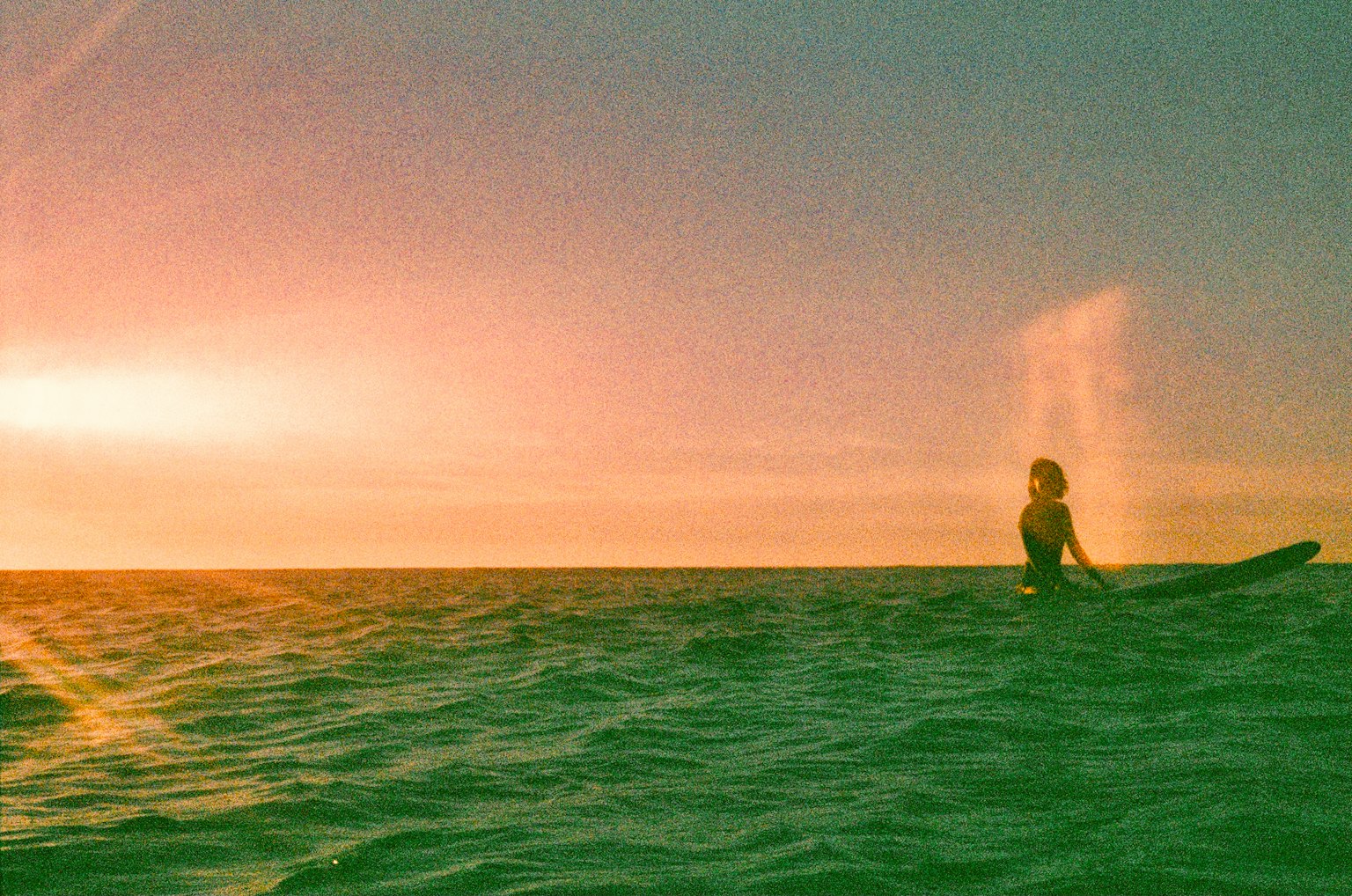 Silhouette einer Frau, die gegen einen Sonnenuntergang surft