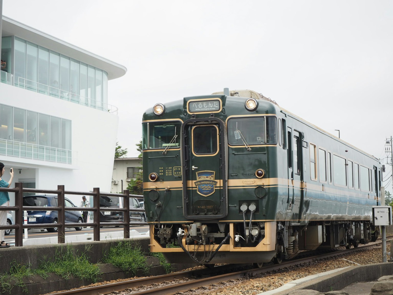 รถไฟโบราณสีเขียวจอดที่สถานีที่มีอาคารสมัยใหม่อยู่เบื้องหลัง