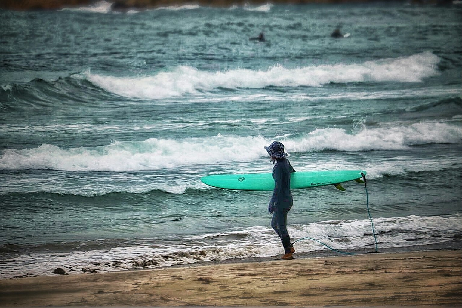 海滩上站着的人手里拿着冲浪板，背景是波浪
