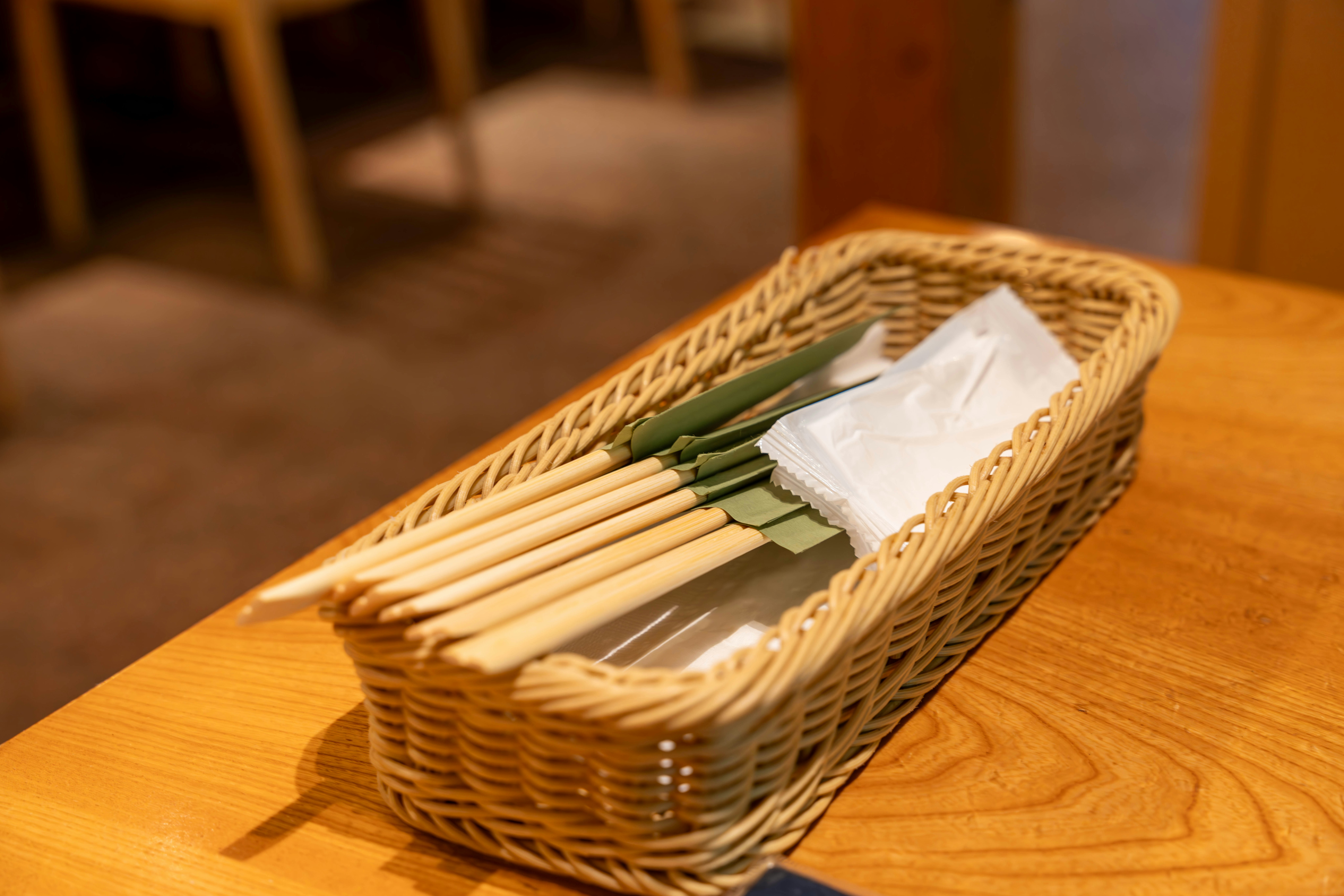 木製テーブルの上の竹かごに入った箸と小袋のセット