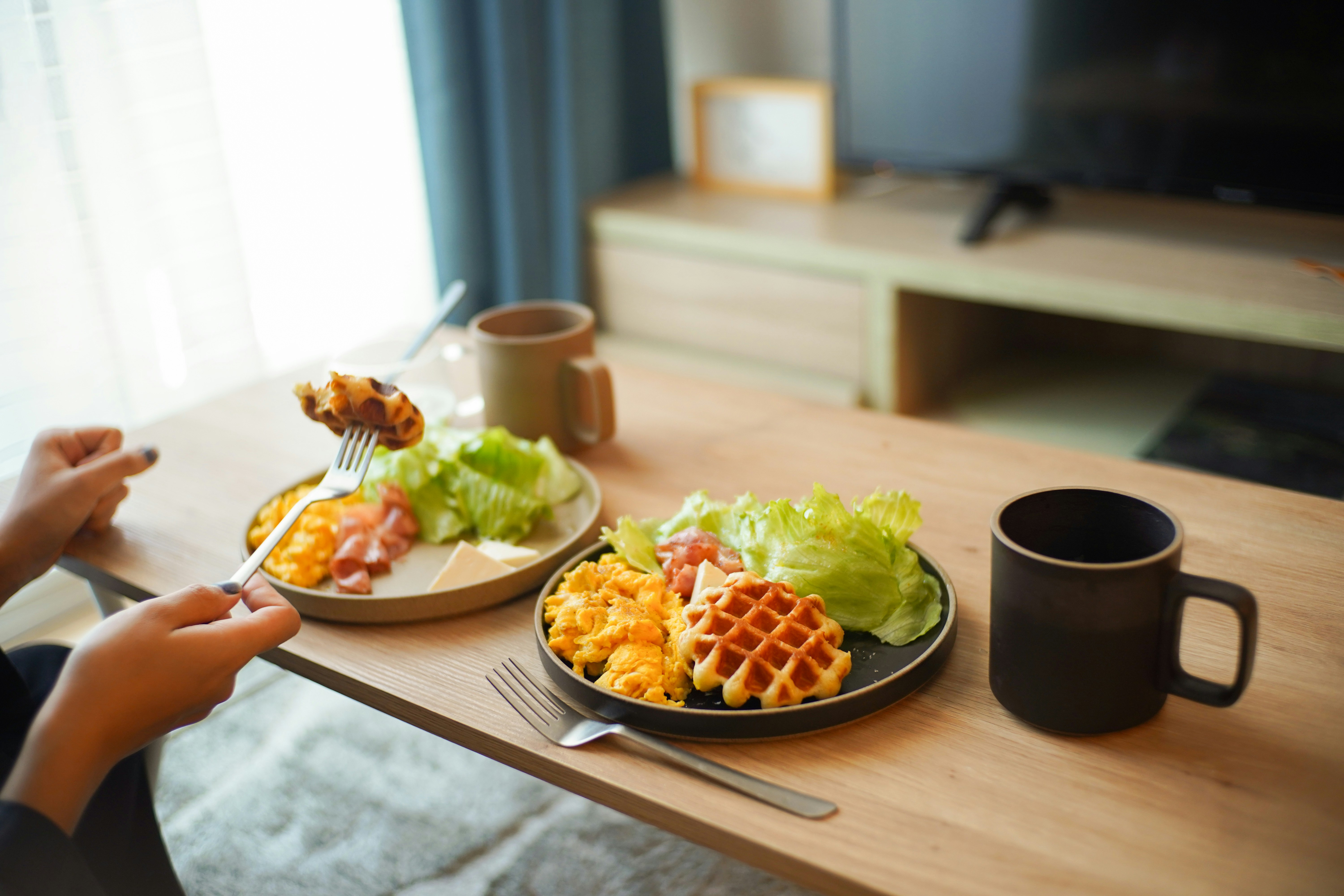 朝食のワッフルとサラダを手に取る家族の食卓
