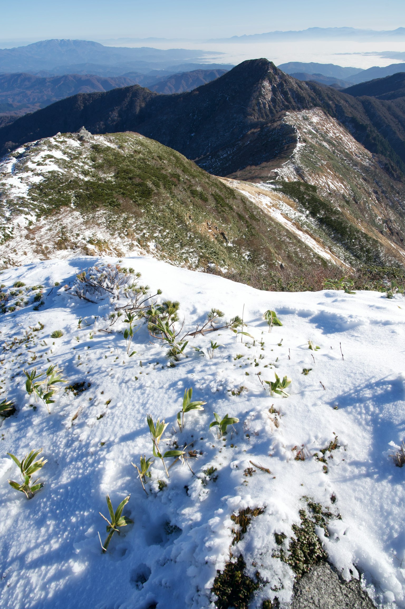 Schneebedeckter Berggipfel mit sichtbaren grünen Grasflecken