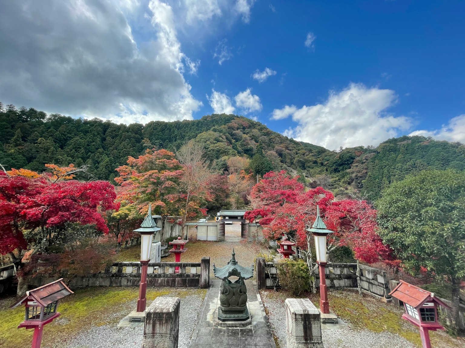 ทัศนียภาพที่สวยงามของวัดที่ล้อมรอบด้วยใบไม้ฤดูใบไม้ร่วงที่มีสีสันพร้อมท้องฟ้าสีฟ้าและเมฆ
