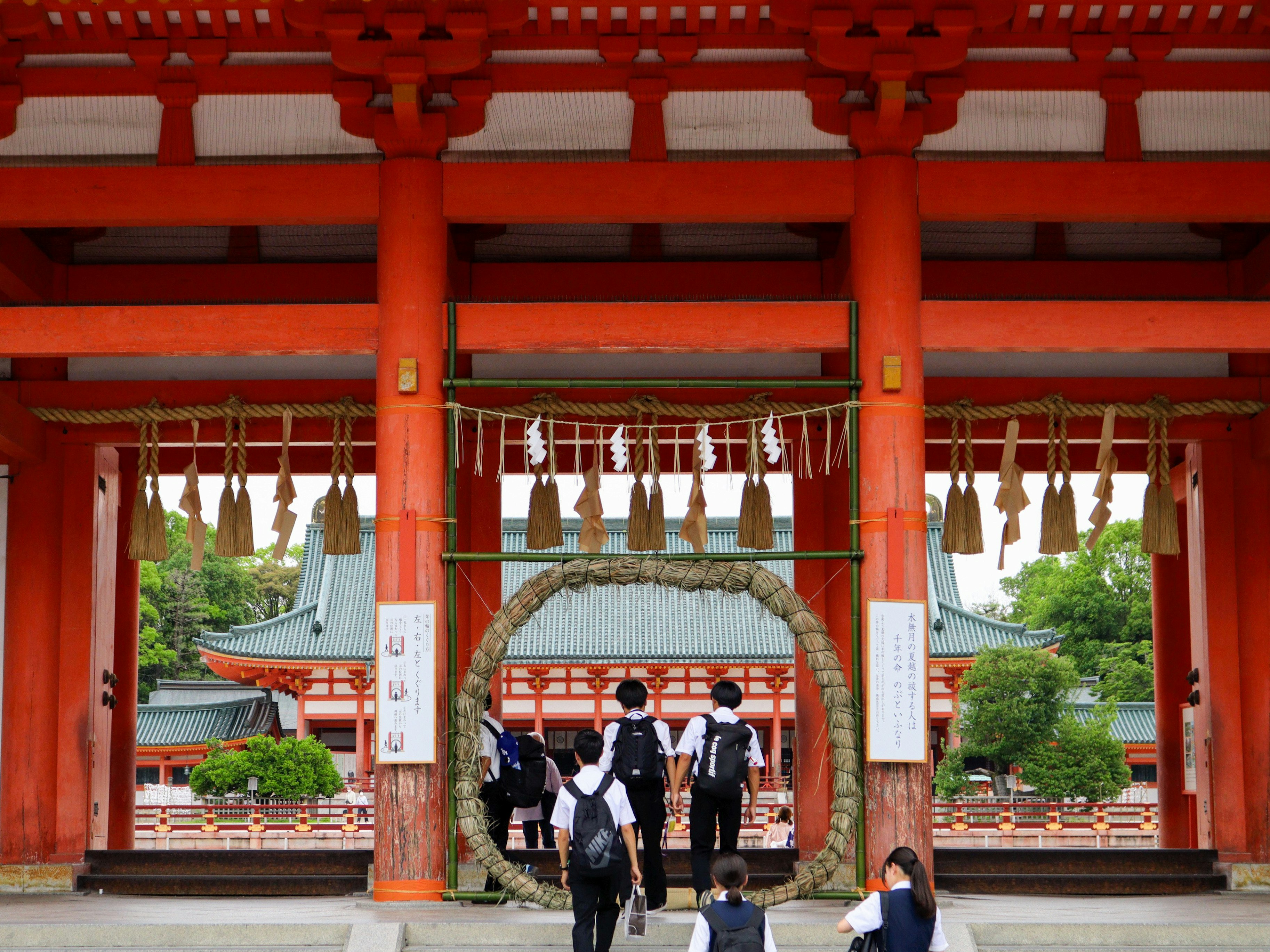 朱塗りの鳥居の下で芽の輪をくぐる参拝者の列