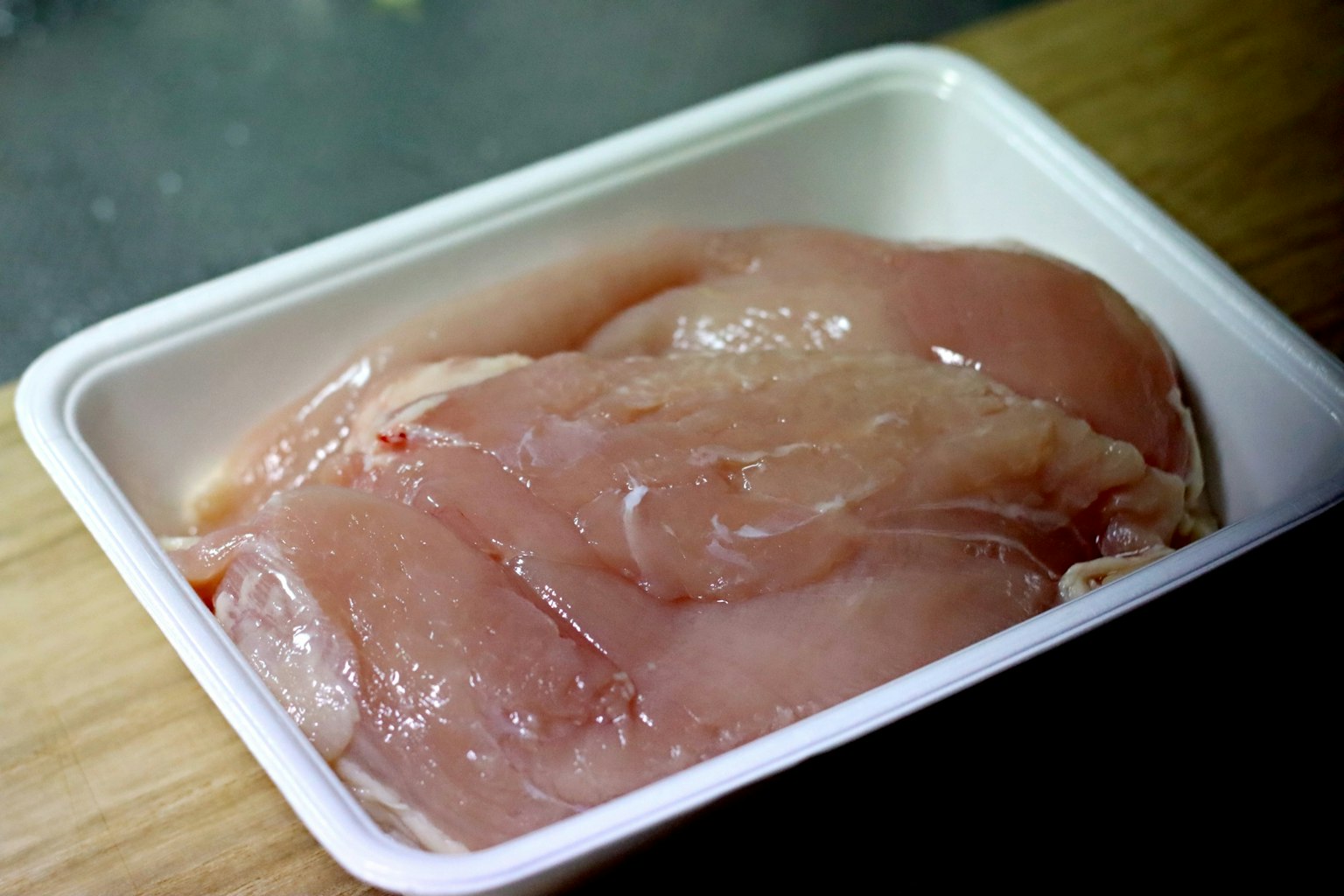 木质台面上的塑料托盘中的生鸡胸肉