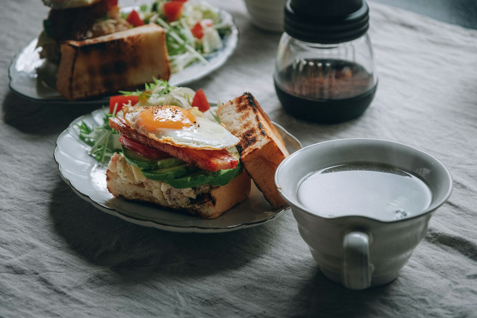Petit-déjeuner avec un sandwich garni d'un œuf au plat et de légumes accompagné d'une tasse de café