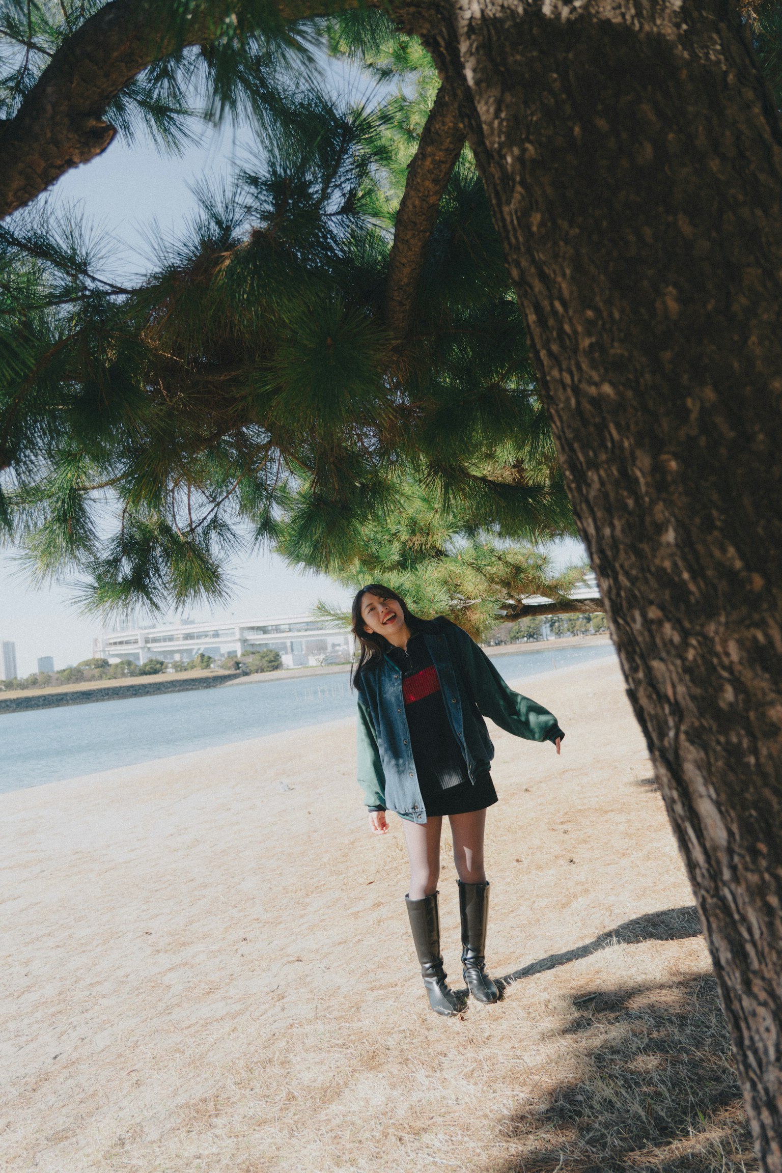 Woman standing under a large tree by the beach Slightly tilted photo Woman wearing a green jacket and boots