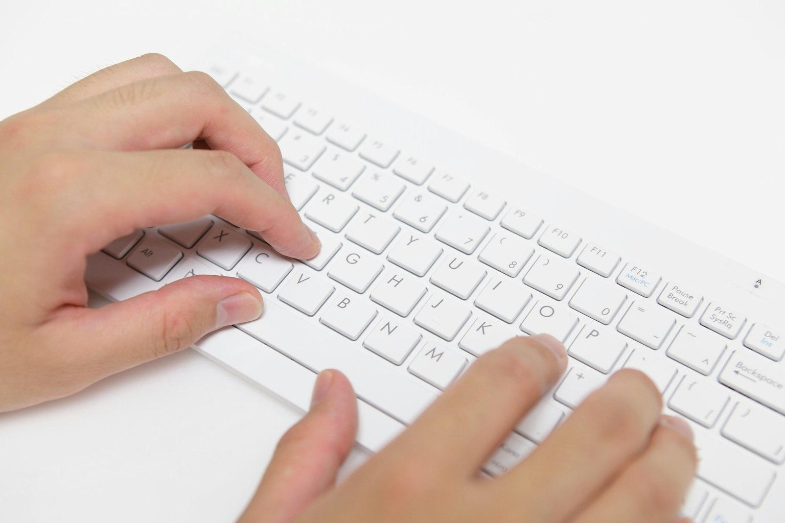 Manos escribiendo en un teclado blanco