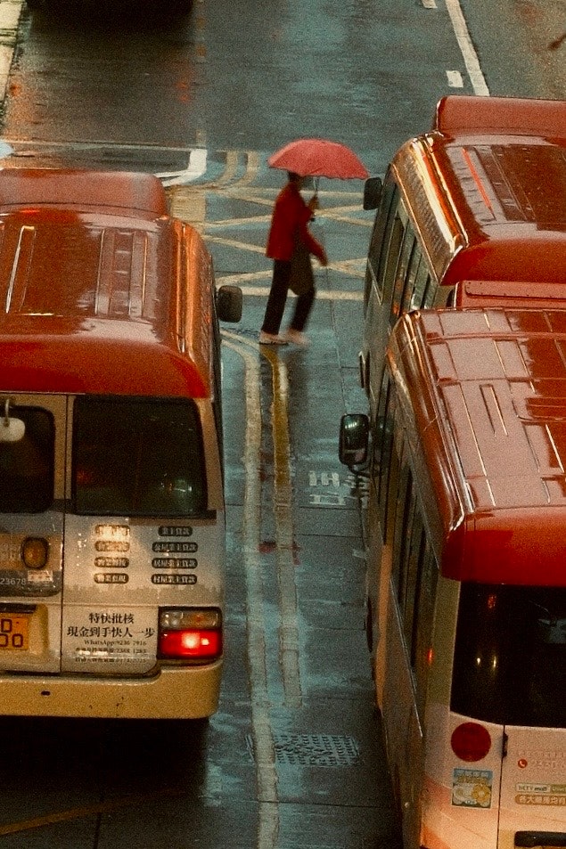 雨の路地で並ぶ赤いバンと傘の人