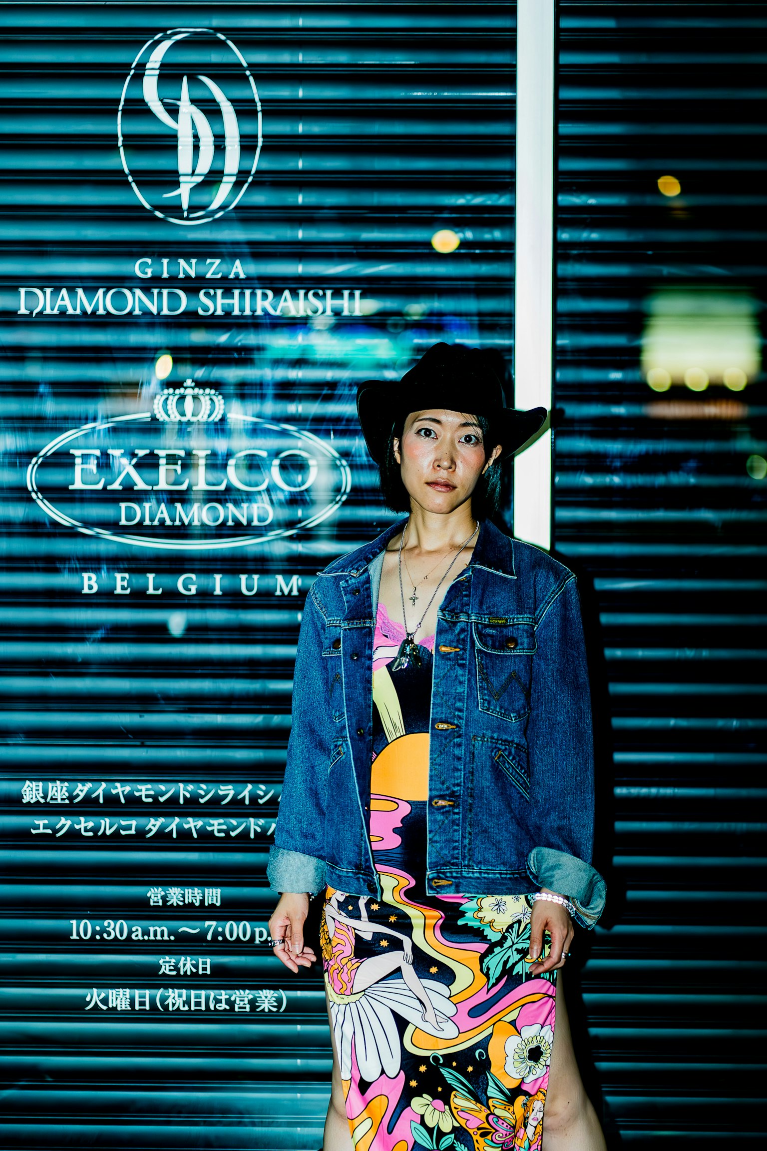 Una donna in un abito colorato e giacca di jeans davanti a un negozio illuminato a Ginza