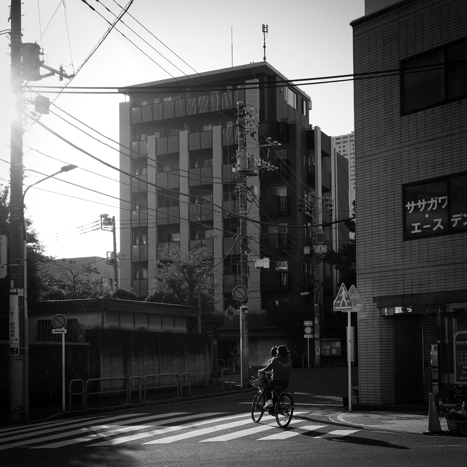 A person riding a bicycle at an intersection with a tall building in black and white