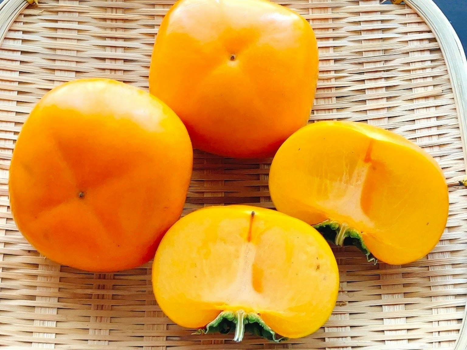Kakis de color naranja colocados en una cesta con uno cortado por la mitad
