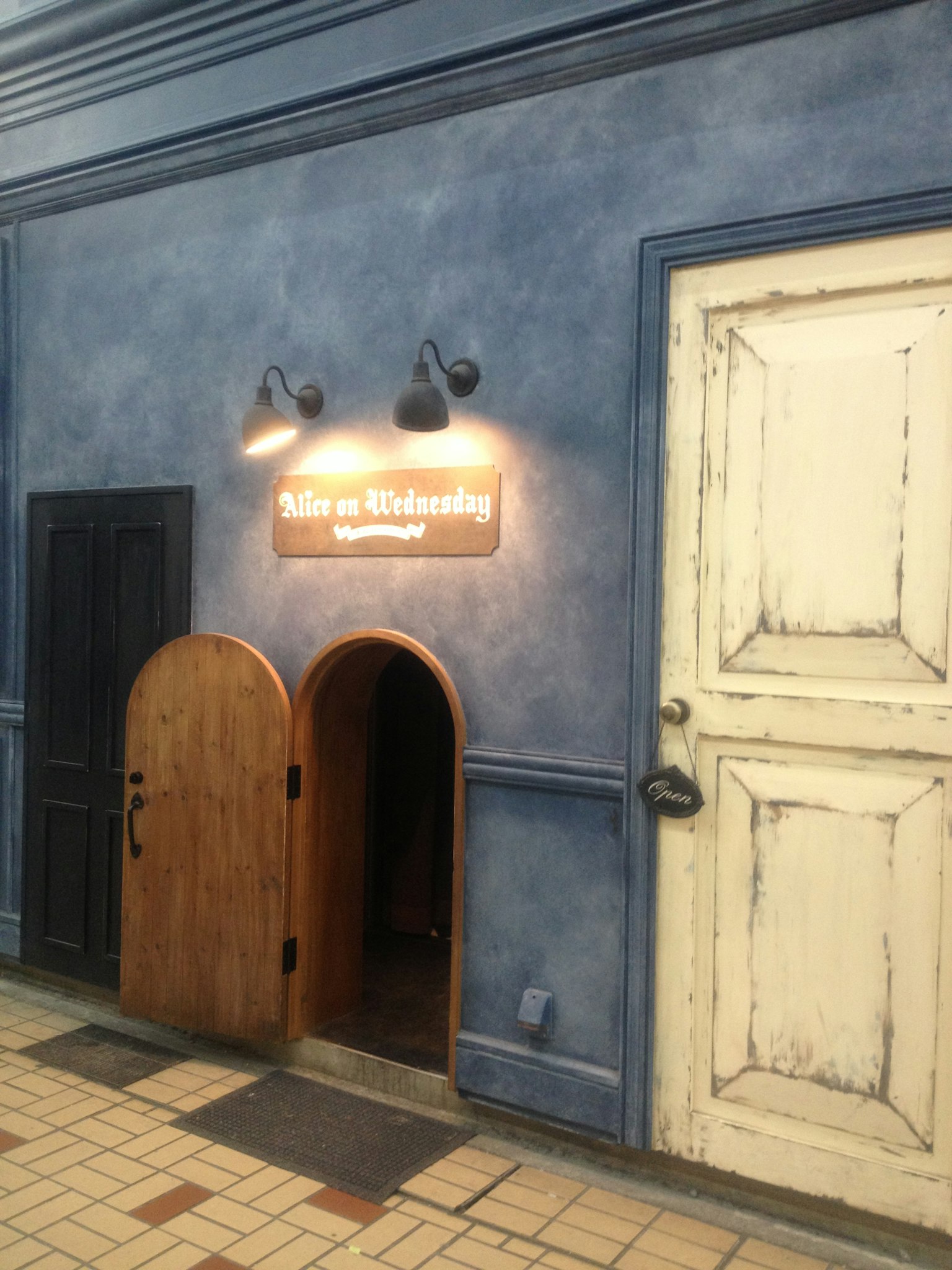 Scène avec un mur bleu présentant une petite porte en bois et une grande porte blanche Un panneau lumineux indique 'With Ability'