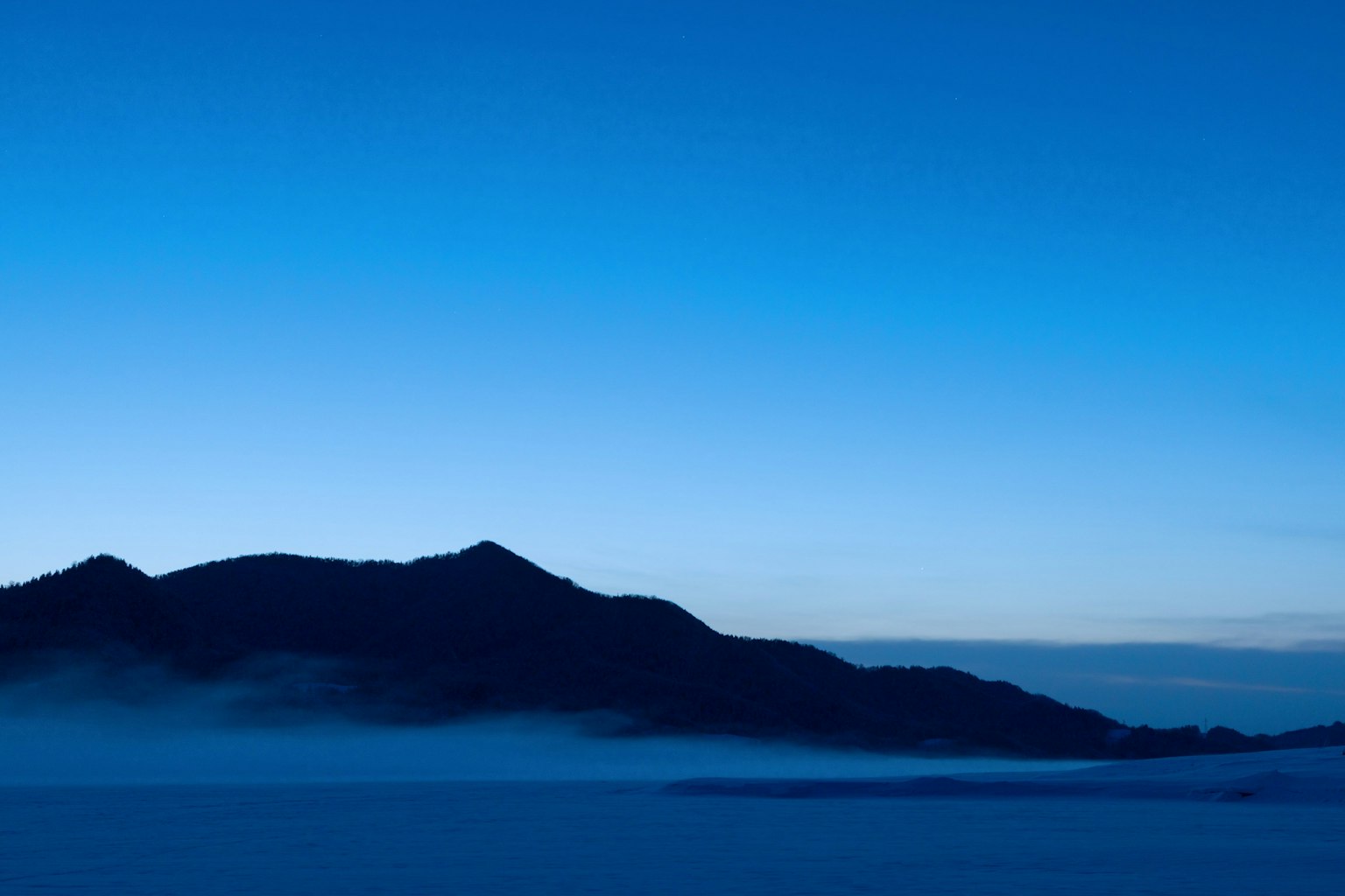Silhouette d'une montagne enveloppée de brume sous un ciel bleu