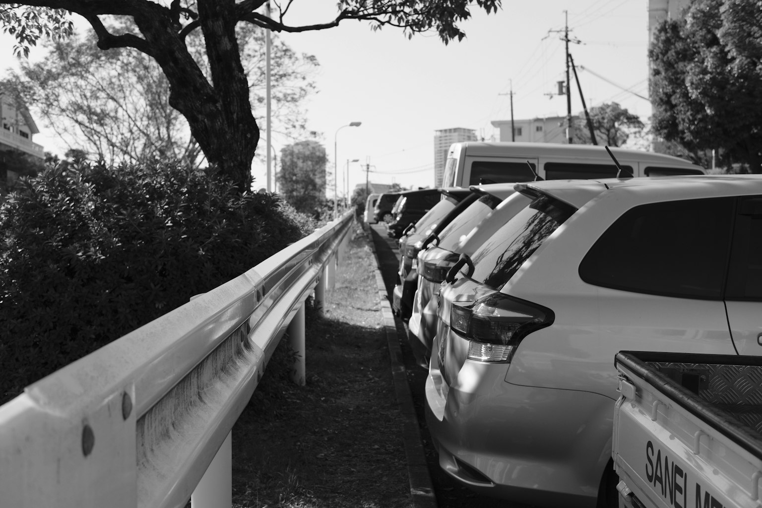 Black and white image of parked cars lined up next to a guardrail