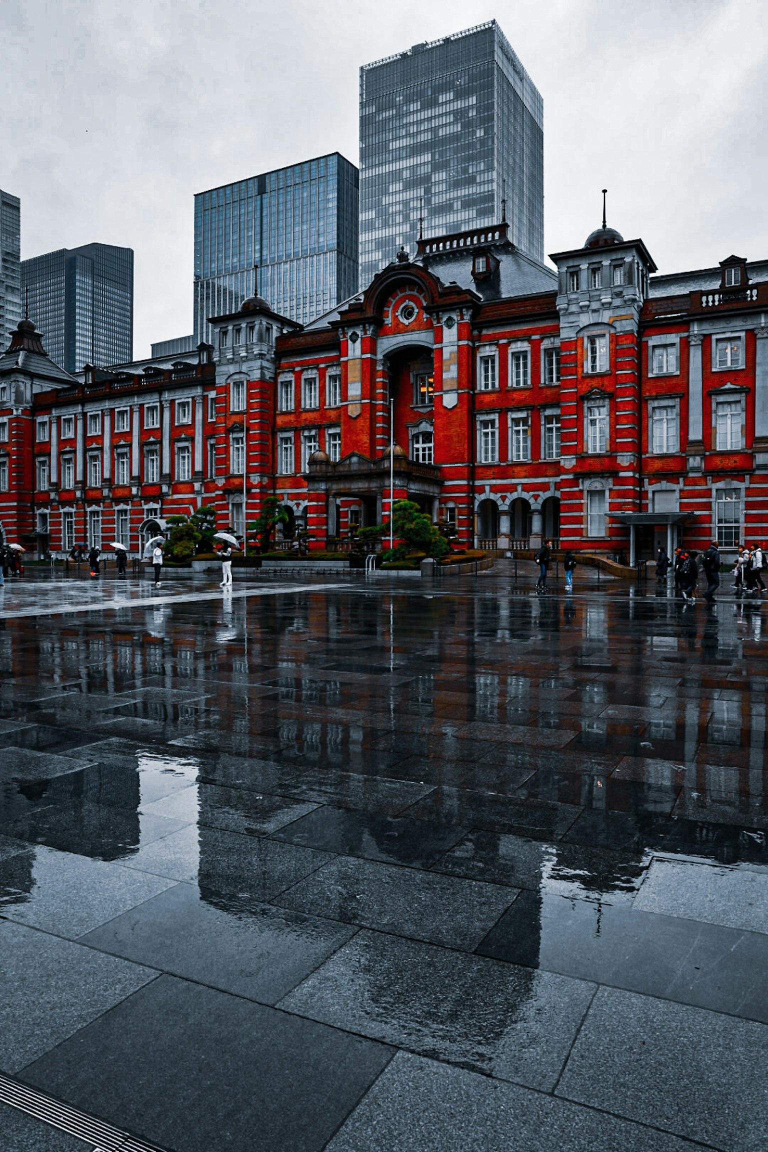 Rotes Backsteingebäude des Tokio Bahnhofs, das sich in Pfützen mit modernen Wolkenkratzern spiegelt