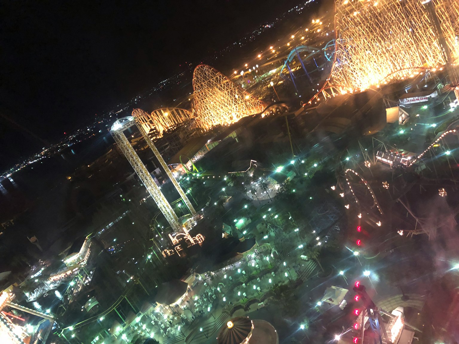 Vista nocturna de un parque de atracciones con luces brillantes y atracciones visibles
