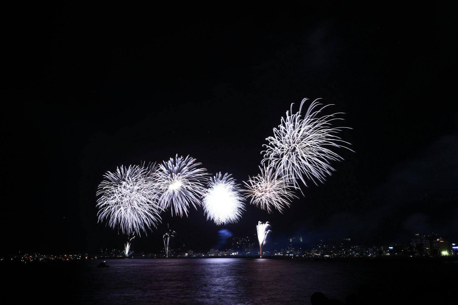 Espectáculo de fuegos artificiales blancos en el cielo nocturno reflejándose en el agua