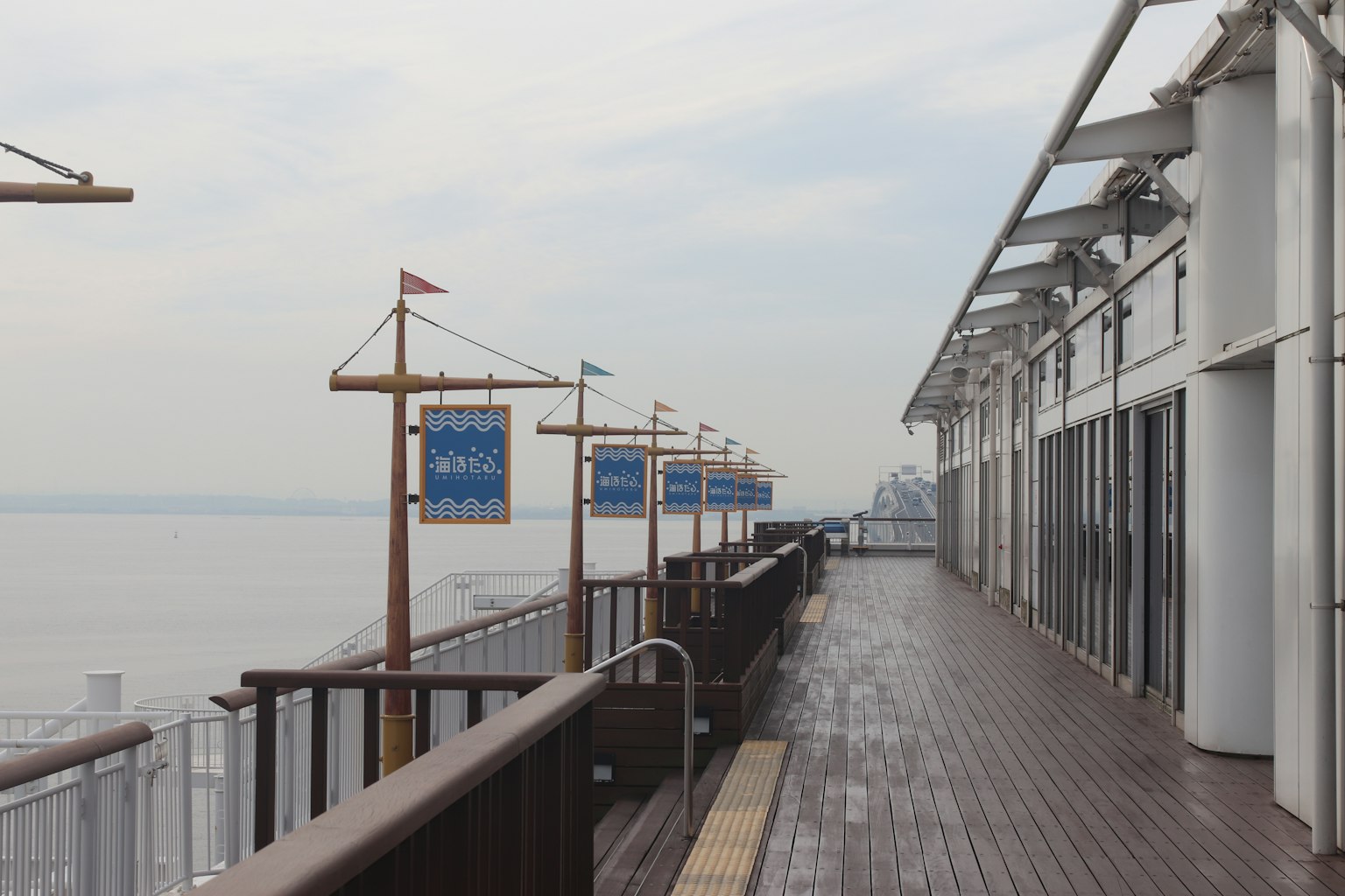 Vue panoramique d'une terrasse donnant sur la mer avec une rambarde en bois et des drapeaux bleus