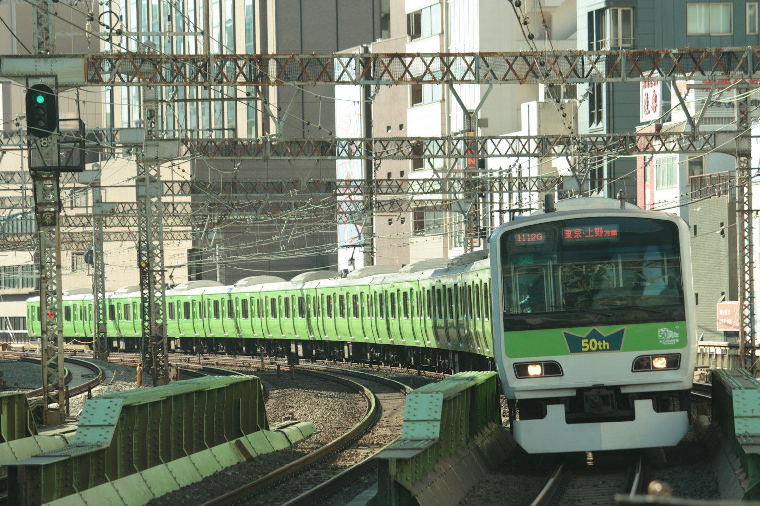 Green train navigating a curve in an urban landscape