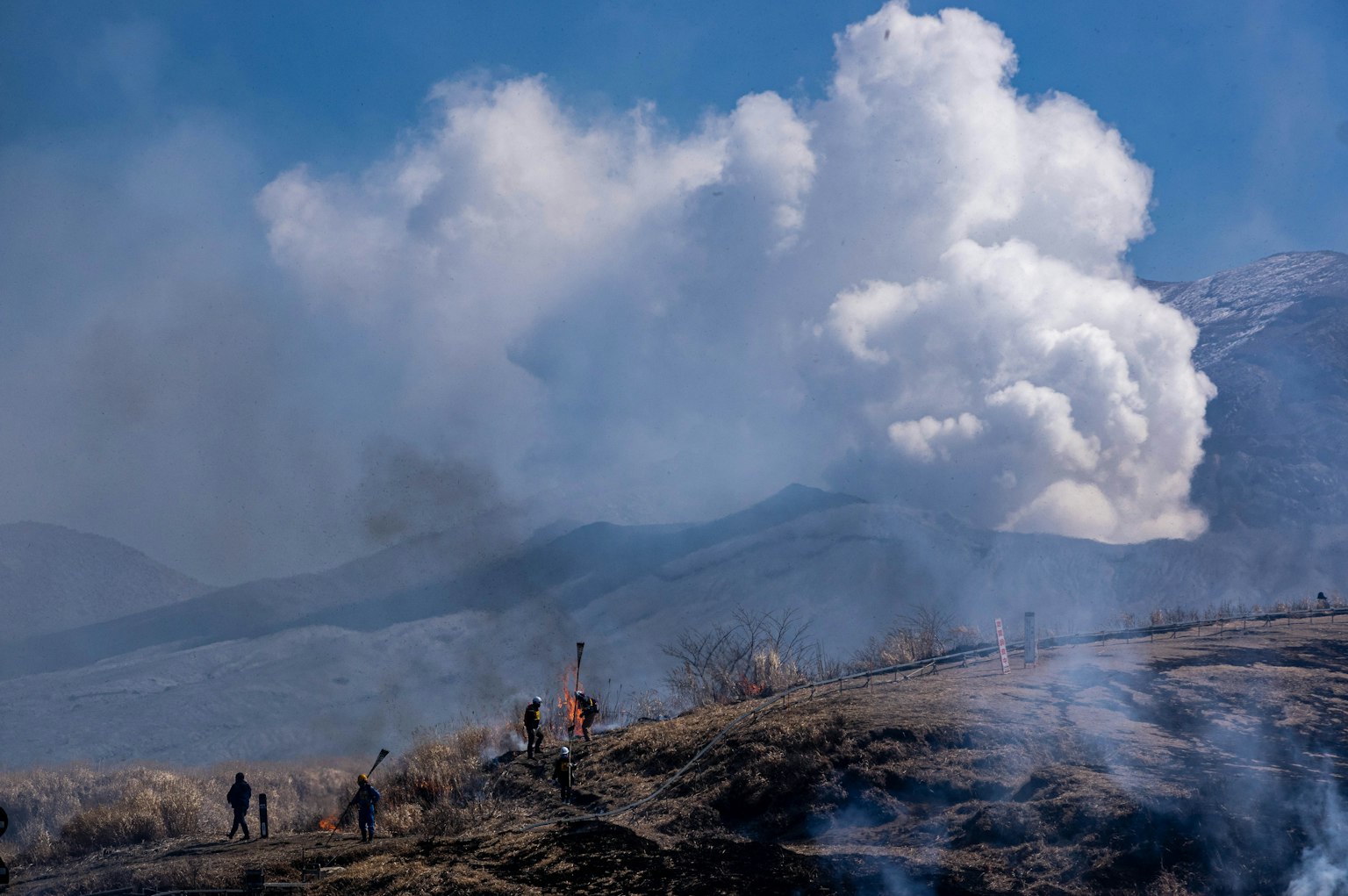 Menschen wandern auf einem Berg mit vulkanischem Rauch im Hintergrund