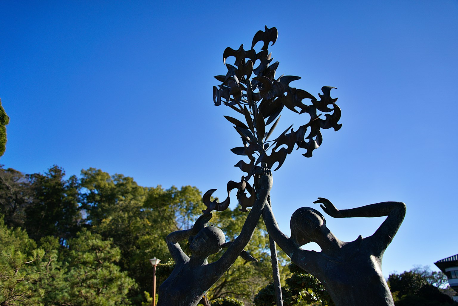 Escultura de dos niños sosteniendo una rama de árbol bajo un cielo azul