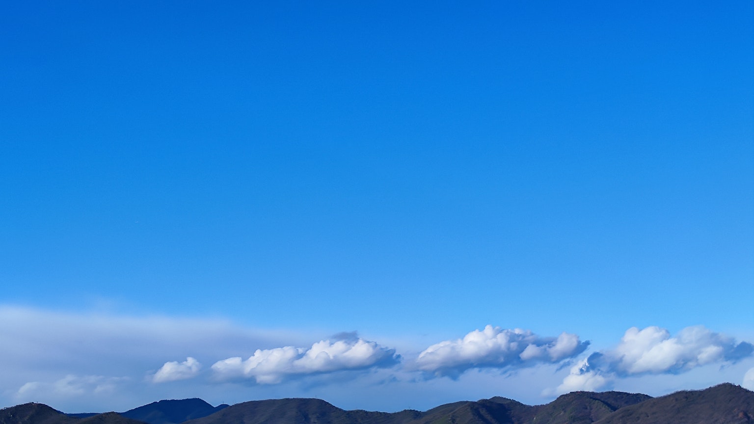 Ciel bleu avec des nuages blancs et des silhouettes de montagnes