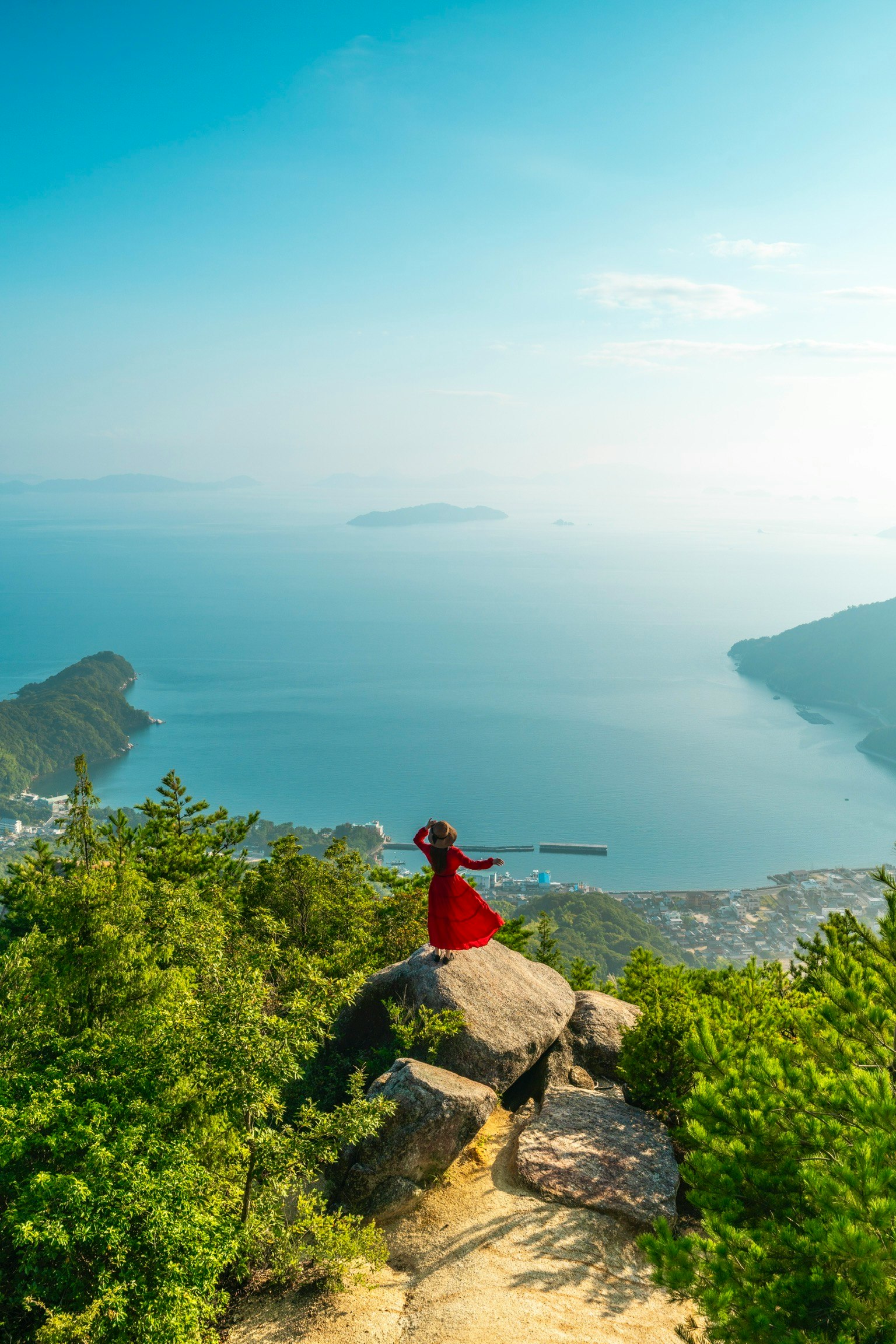 美しい海の景色を背景に赤い衣装を着た人物が岩の上に立っている