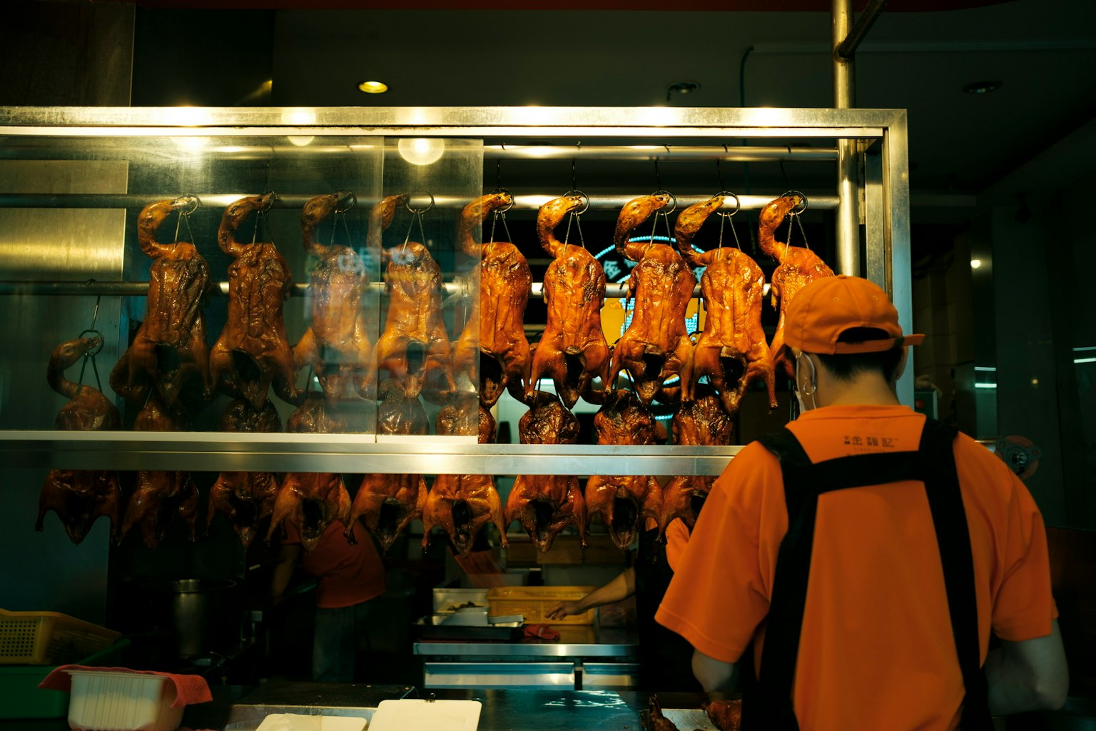 Ein Arbeiter in orangefarbener Uniform verkauft Hähnchen vor einem Glaskasten mit hängenden Hähnchen