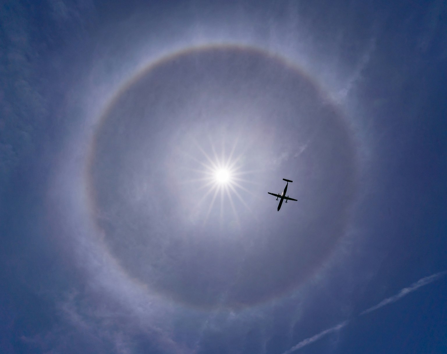 Avión volando contra un halo brillante del sol en el cielo azul