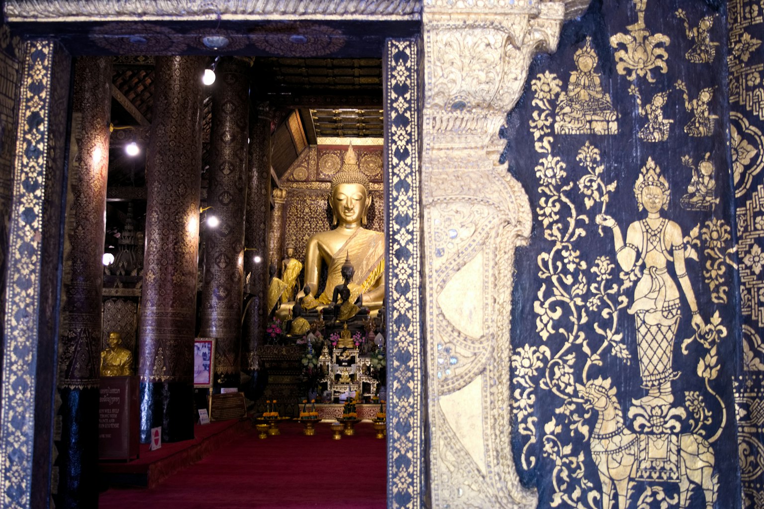 Interior de un templo con una estatua de Buda dorada y paredes decoradas intrincadamente