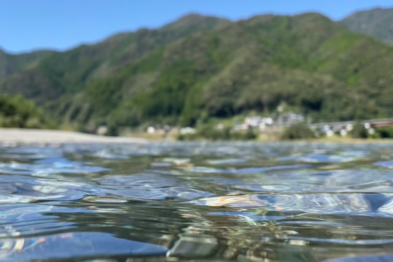 Underwater view of clear water with green mountains in the background