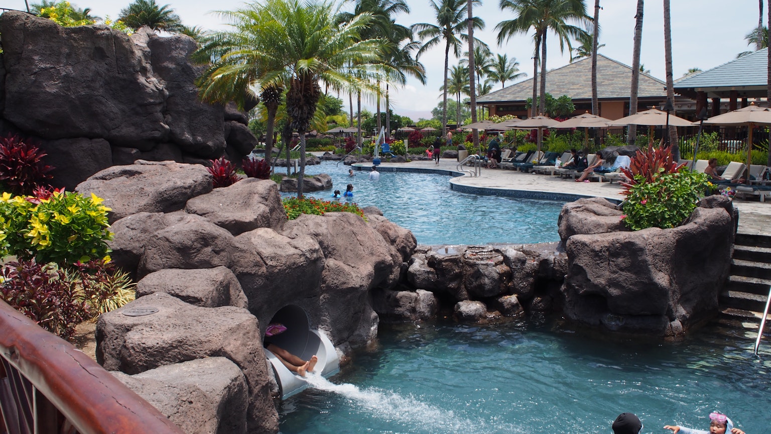 Area della piscina del resort con formazioni rocciose e palme in un'atmosfera soleggiata e rilassante