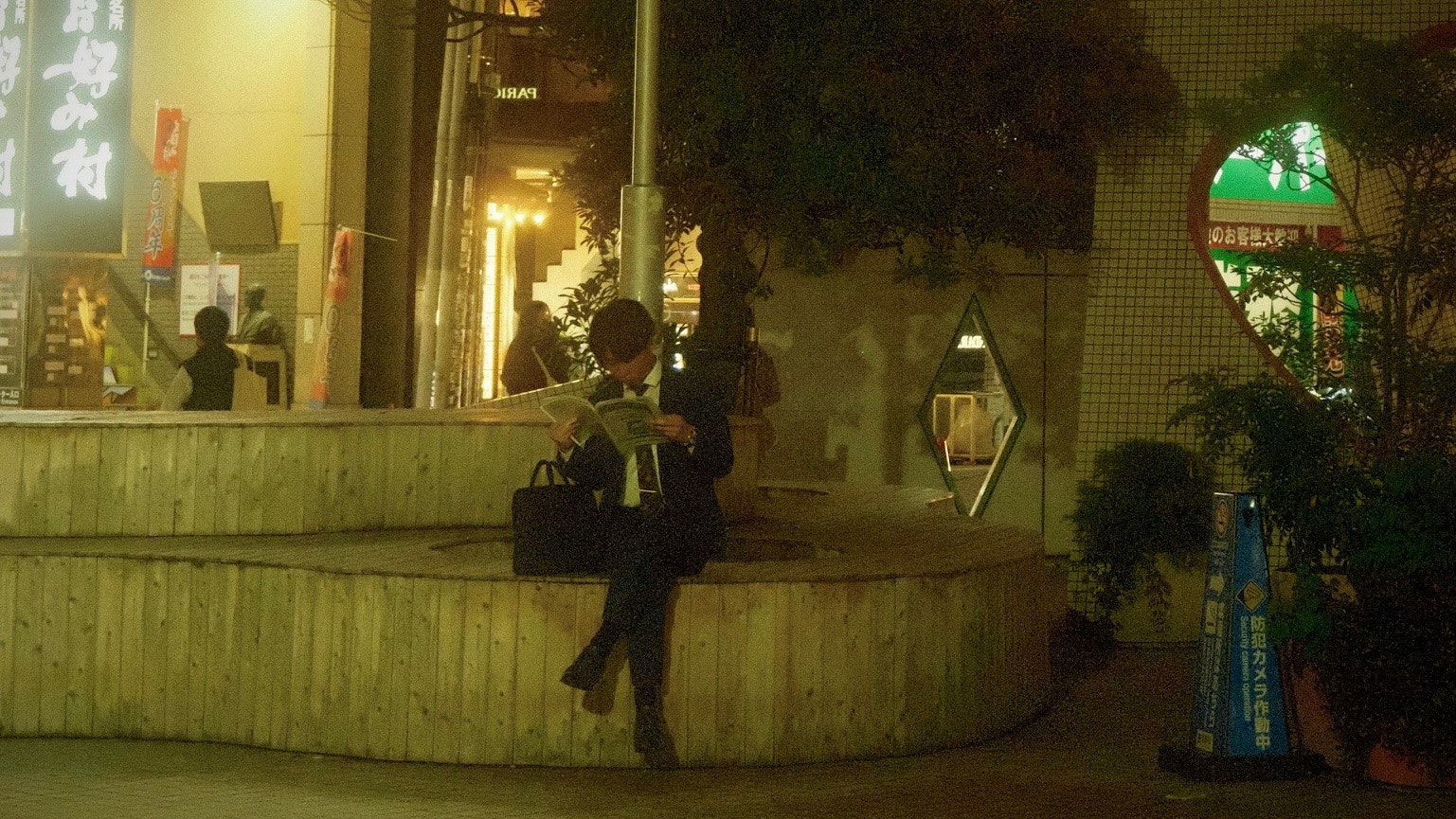 夜の街角で立ち話する人々と街灯の光が差す路地の風景