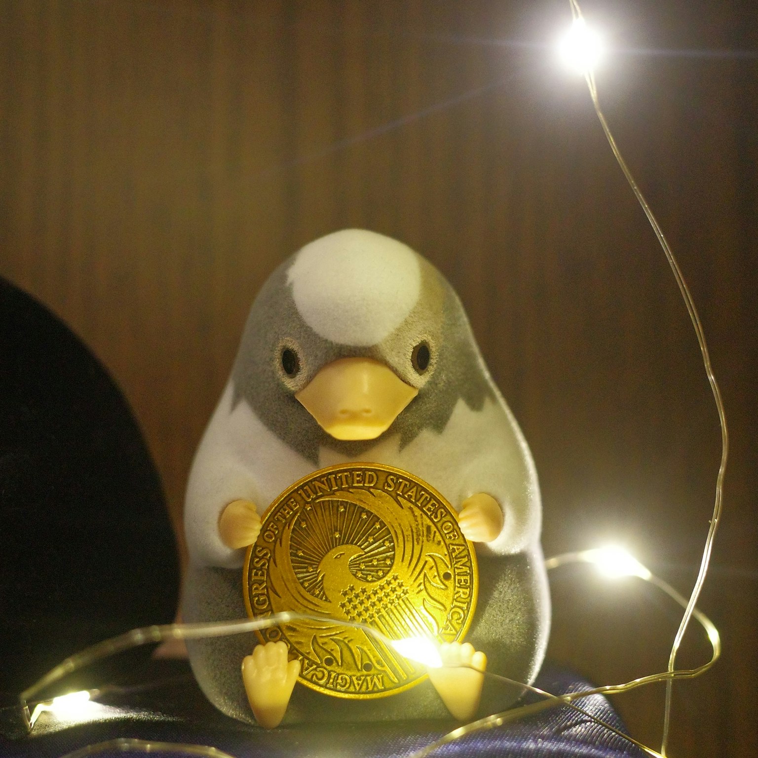 小さなペンギンのフィギュアが金色のコインを持ち、周りに小さなライトが飾られている