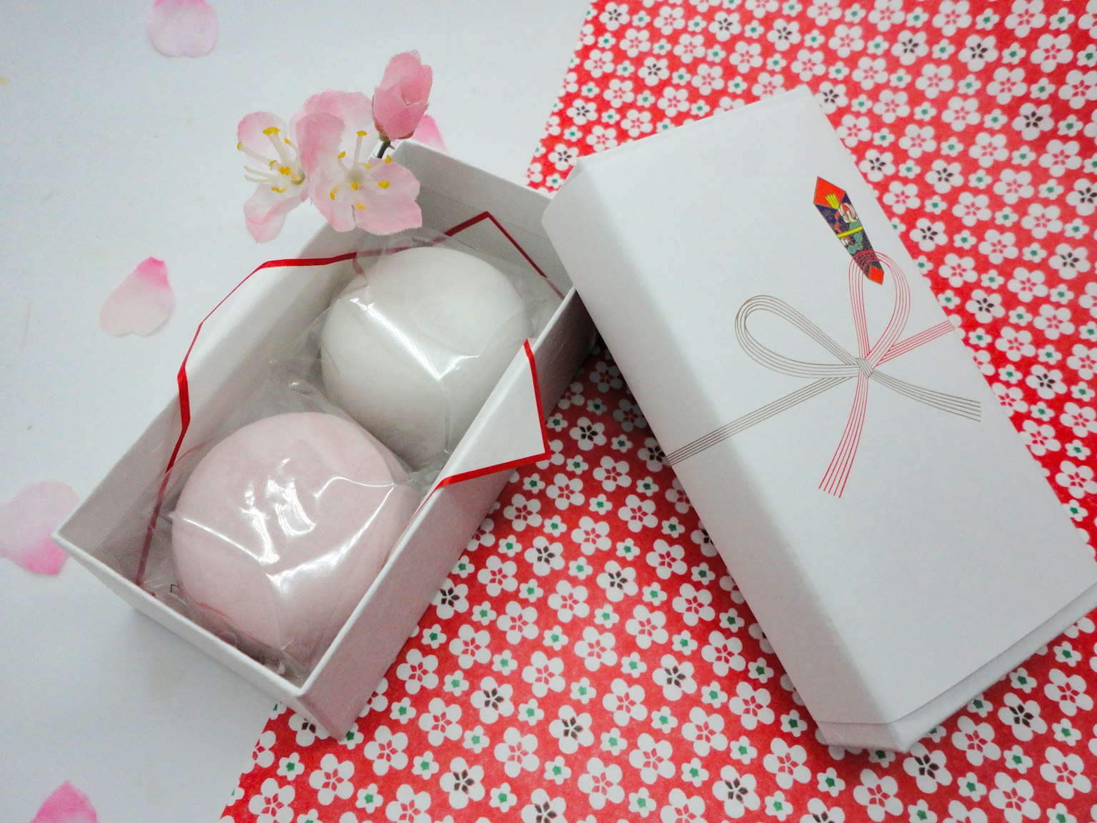 Une boîte blanche contenant des sucreries japonaises rose et blanche avec des pétales de cerisier
