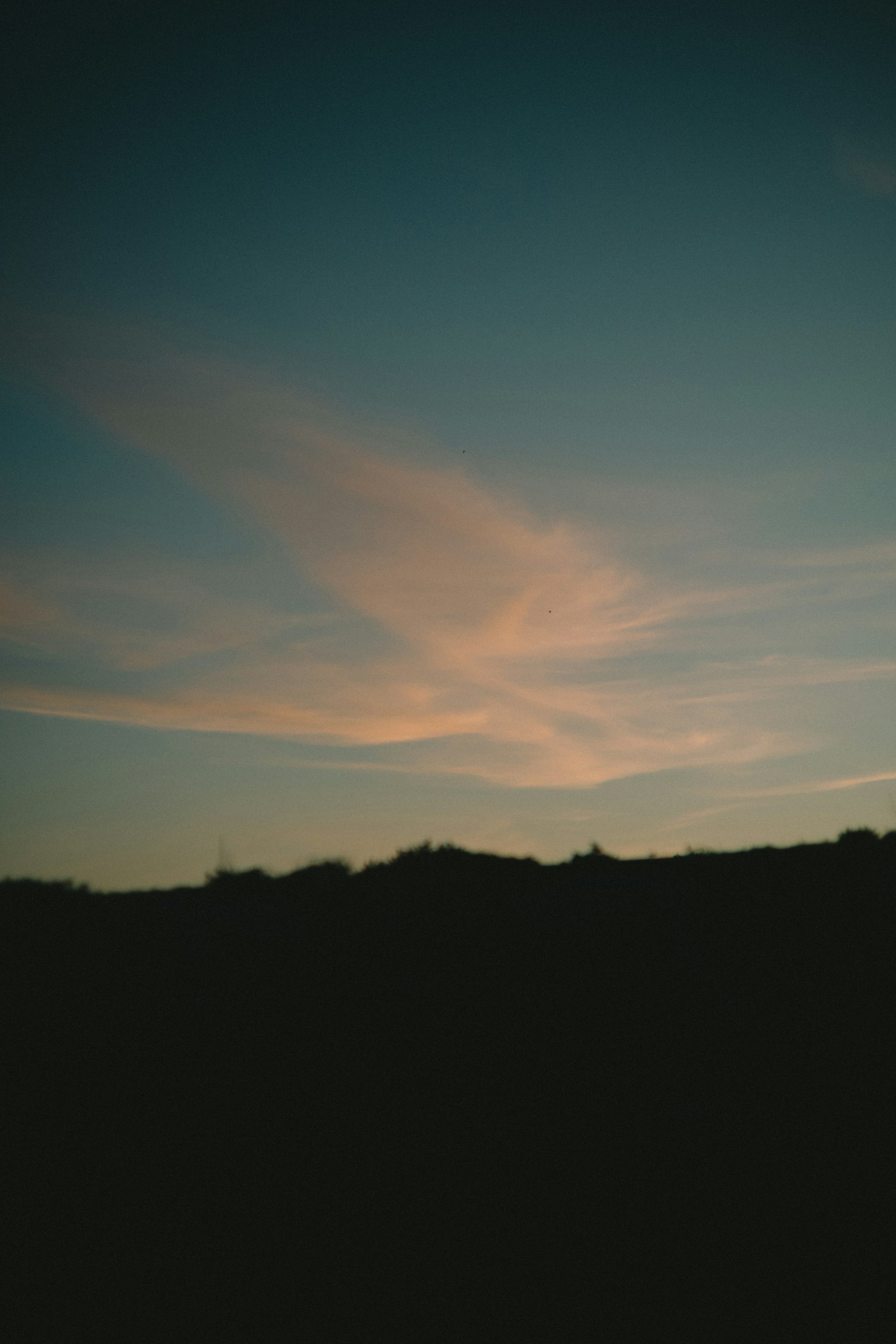 Soft clouds in a blue sky with silhouetted hills