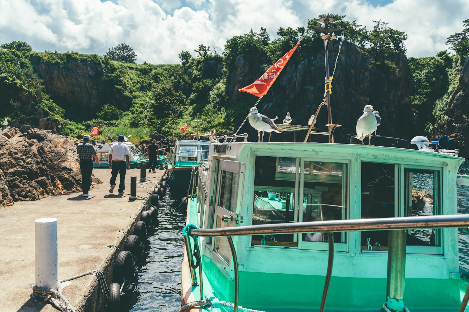Pemandangan indah sebuah perahu hijau berlabuh di pelabuhan dengan orang-orang yang beraktivitas
