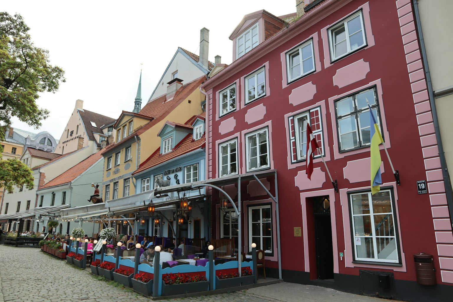 Bunte Gebäude entlang einer Straße mit einer Café-Terrasse und sichtbaren Fahnen