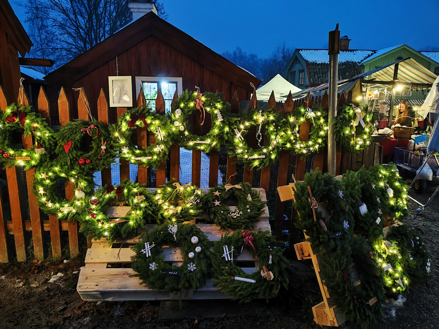 Coronas de Navidad exhibidas en palets de madera frente a una cabaña