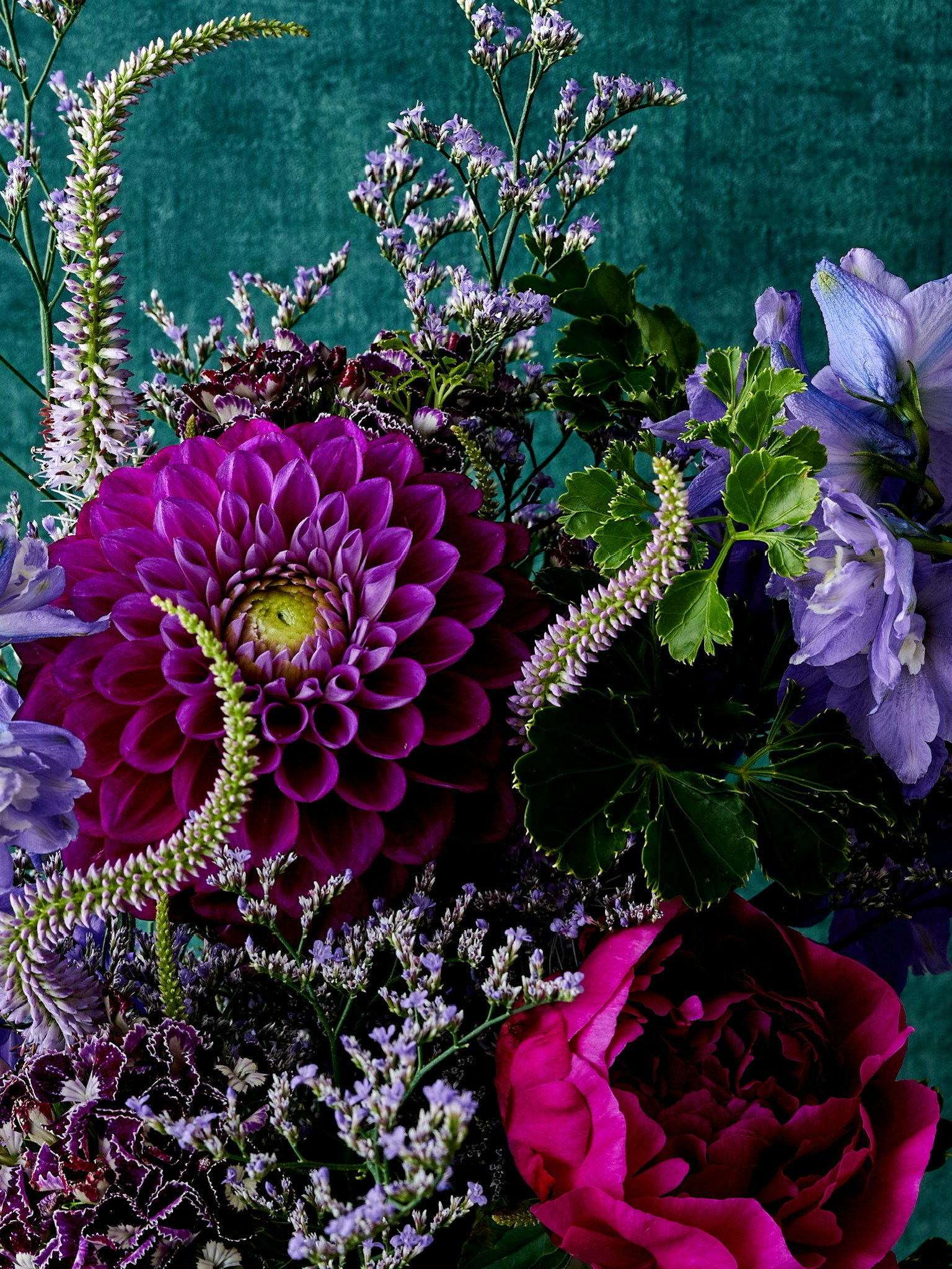 Arrangement floral avec une dahlias et une rose violettes sur fond vert avec diverses fleurs et feuillages