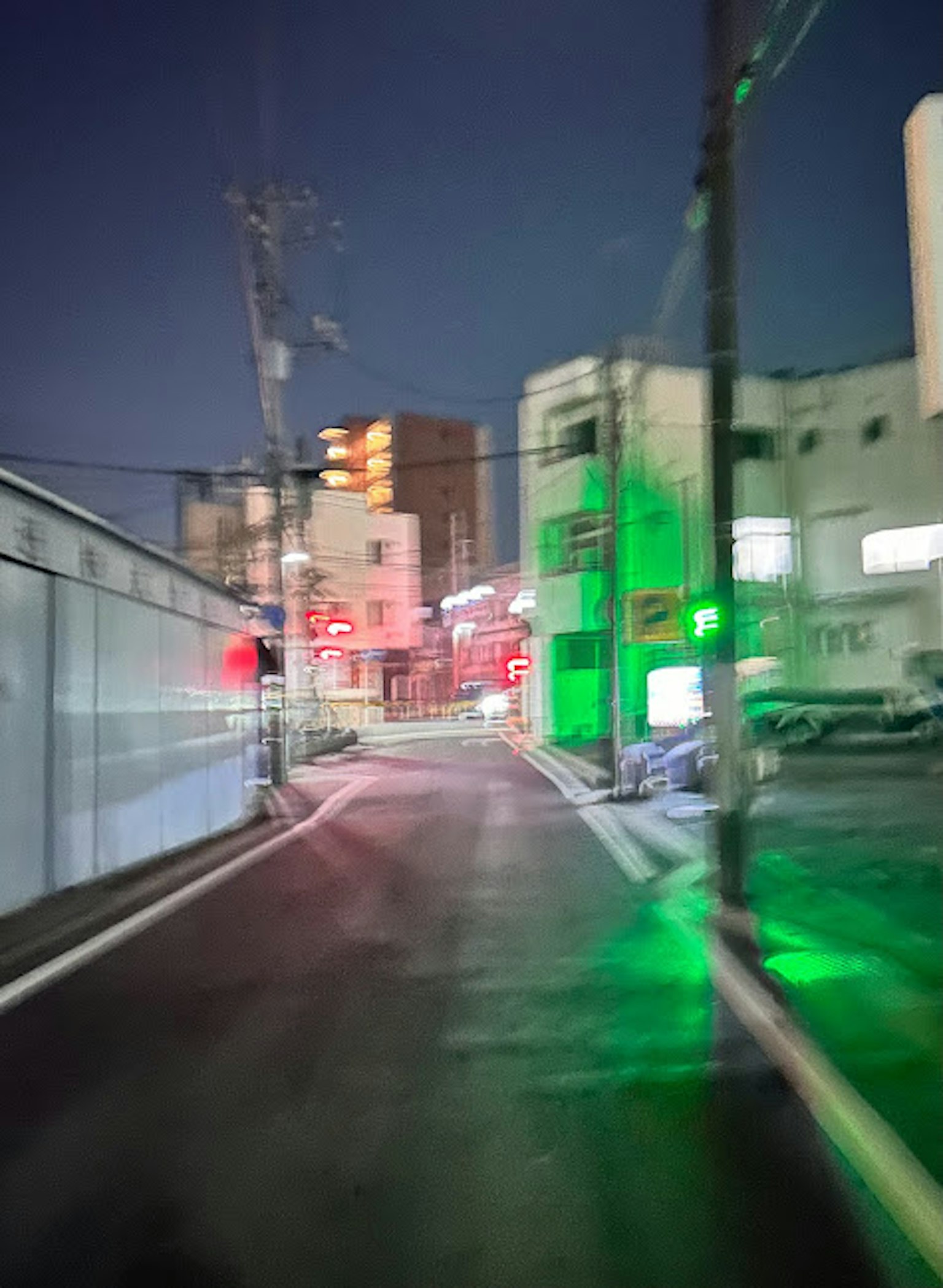 模糊的夜間街道場景，帶有綠色燈光和紅色交通信號