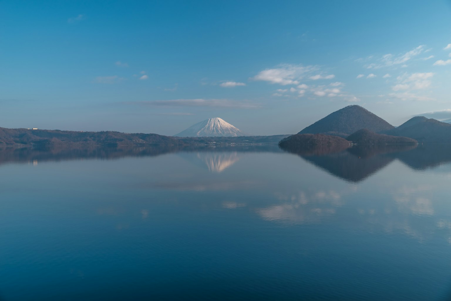 Scenic view of a calm lake reflecting Mount Fuji under a blue sky