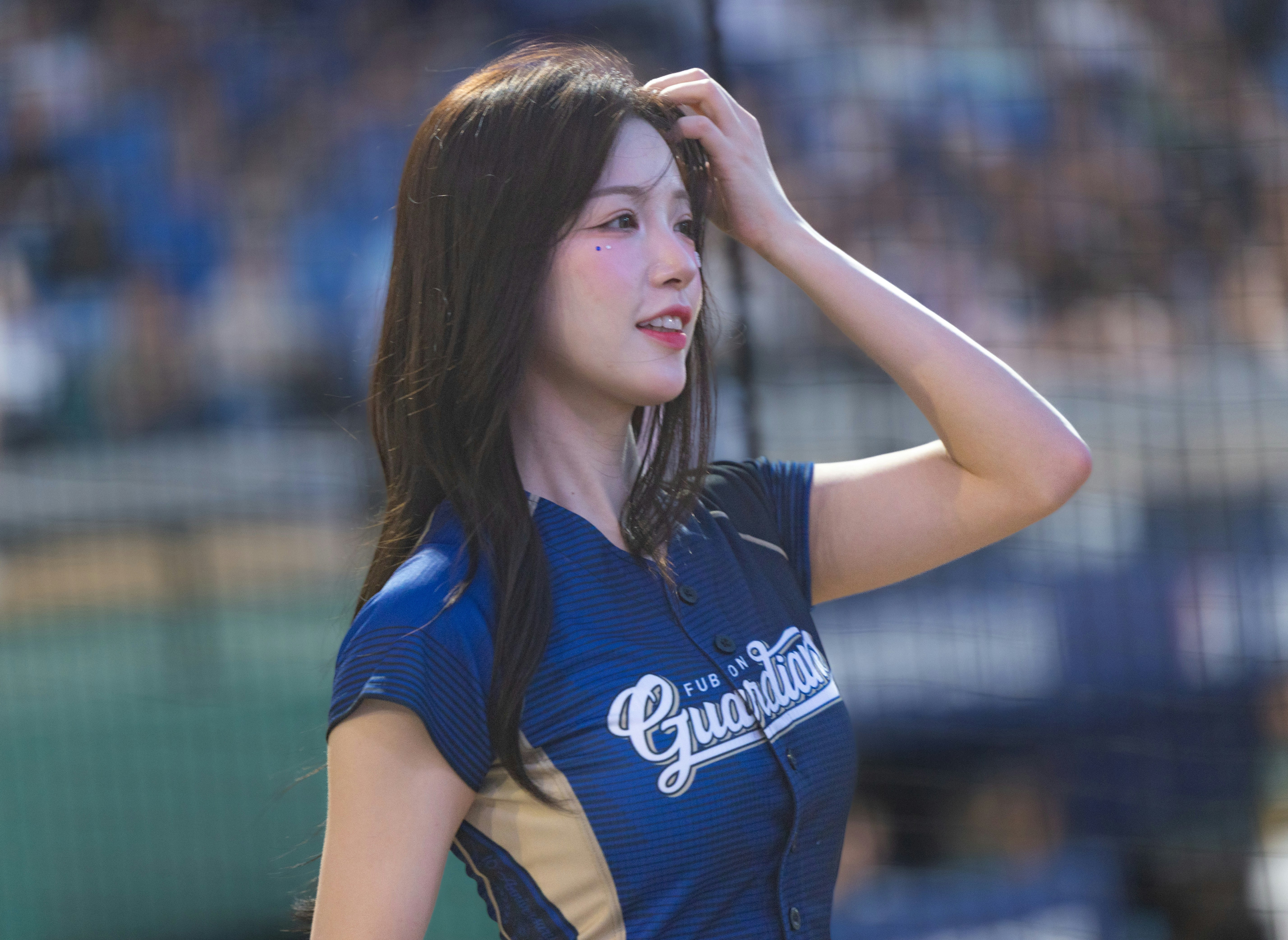 青いユニフォームを着た女性が手で髪を整える屋外の横顔