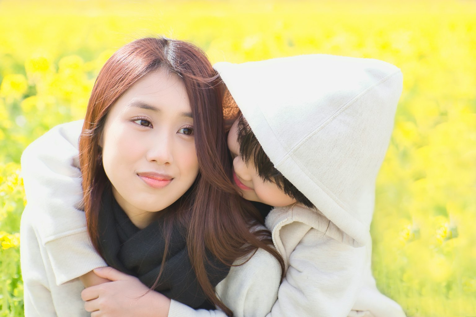 一位女性在黃色花田中微笑，孩子抱著她